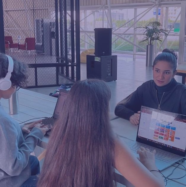 Two people working together at a table with a laptop, water bottle, and blurred background of an indoor workspace